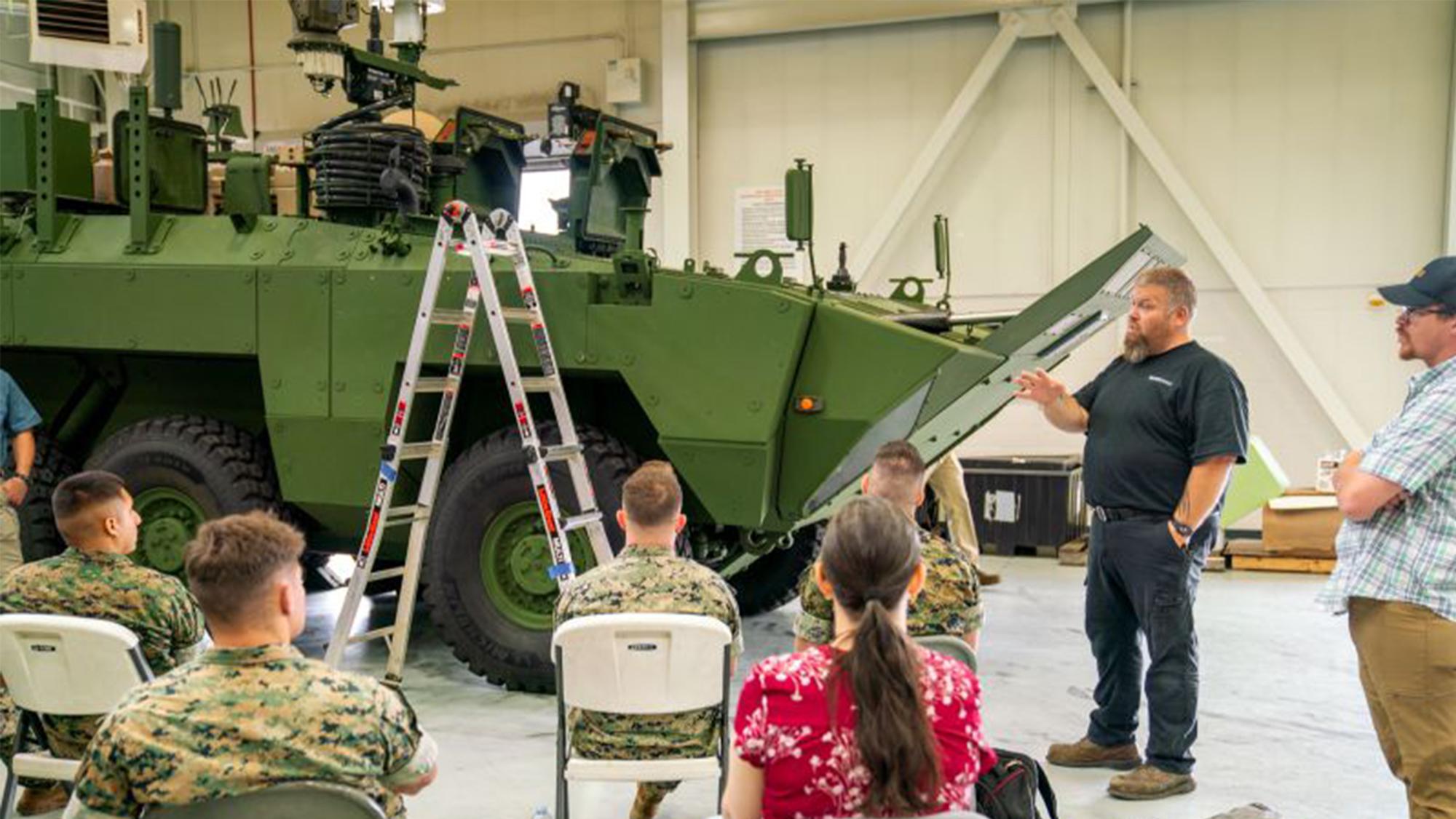 ARV in a warehouse with people sitting and listening to a man present.